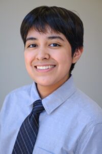 Headshot of Lira Amari Ramirez. Latino young adult with short black hair wearing a grey button down shirt.